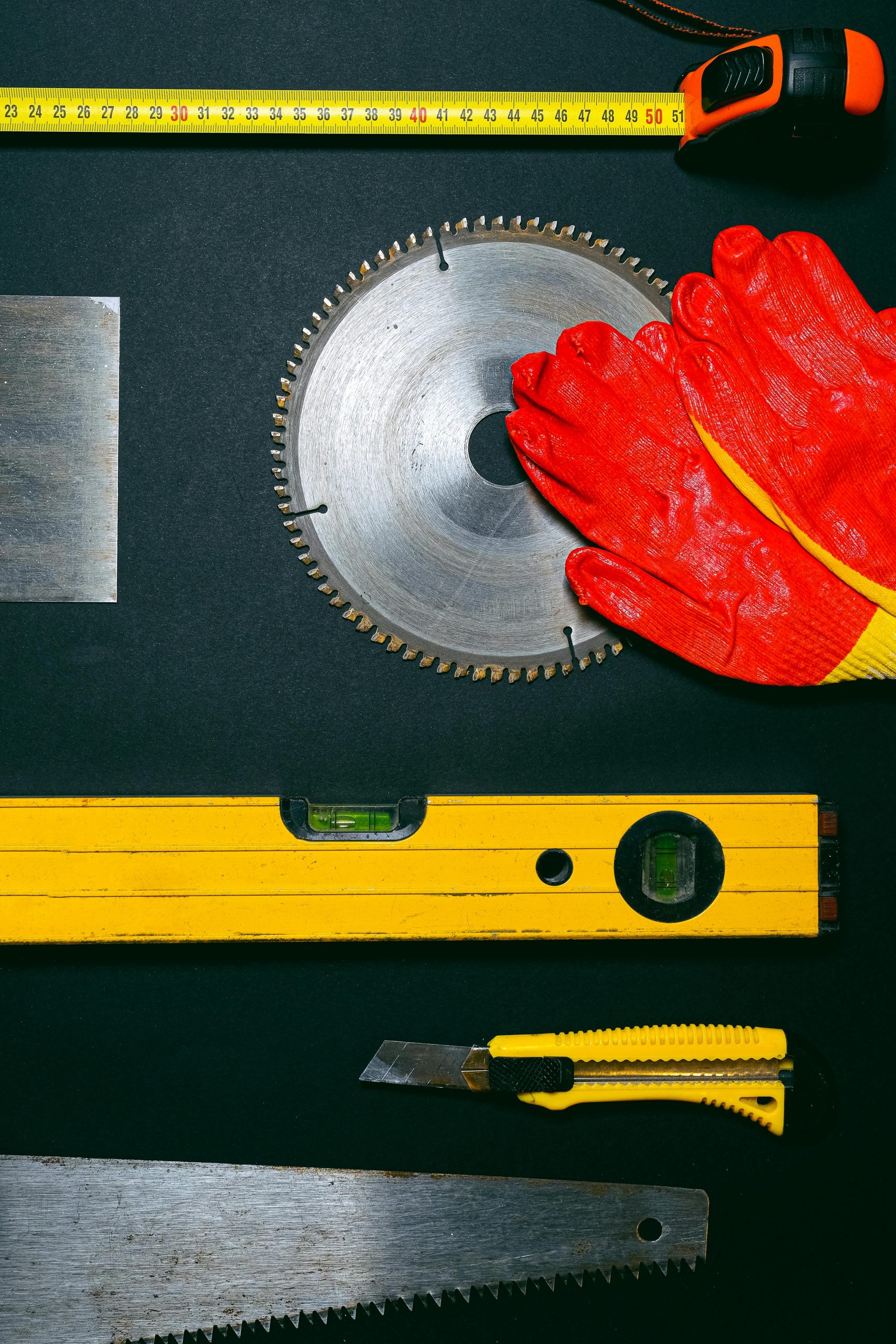 Collection of construction tools including saw blade and gloves on a black surface.